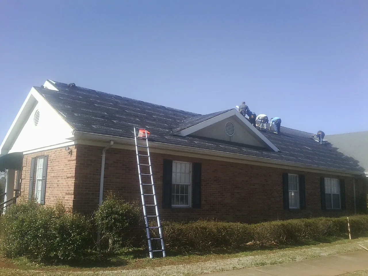 Crew tearing shingles off a brick ranch roof with a ladder set — Metal Roof Repair work by our crew in Freehold