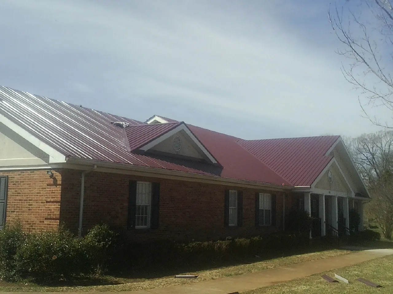 Red metal roof with gabled entries on a long brick building, from a Hail Damage Roof Repair job in Freehold
