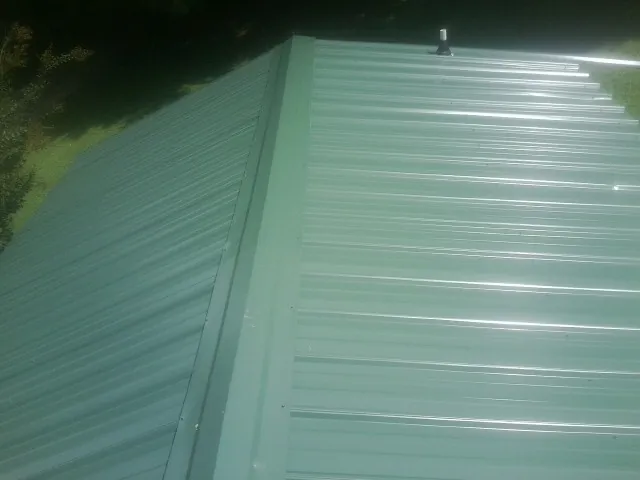 New green metal panels meeting at the ridge of a roof — Flat Roof Repair work by our crew in Freehold