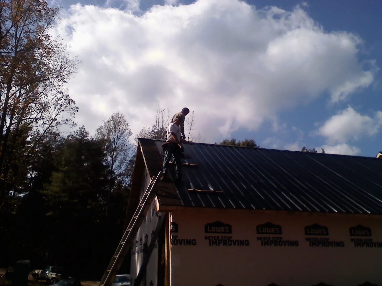 Roofer fastening dark metal panels high against a cloudy sky, from a Roof Inspection job in Freehold