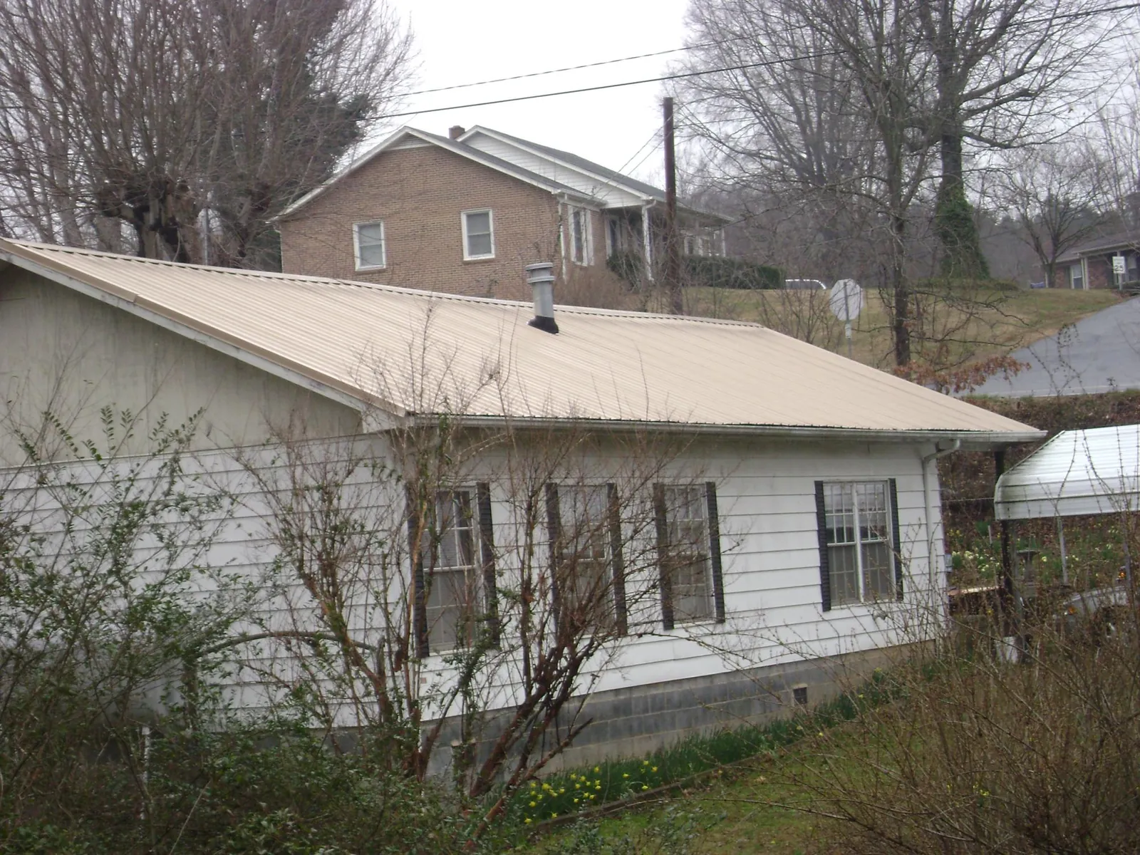 Tan metal roof on a white sided house set into a hillside — Commercial Roofing by Roofing Brothers in Freehold